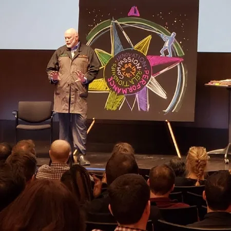 Richard Hight speaking to an audience beside a painted star artwork